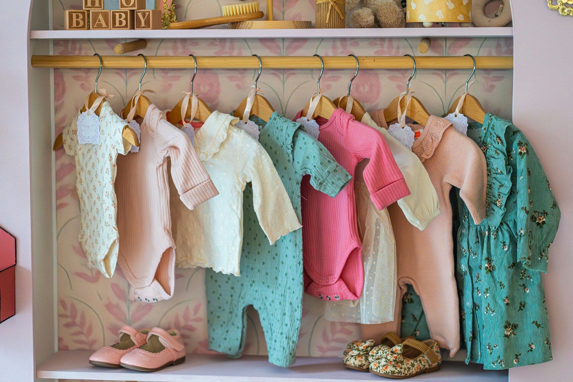 Baby clothes on wooden hangers above rows of small shoes